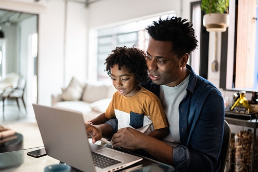 Father using the laptop with son at home searching for health insurance.
